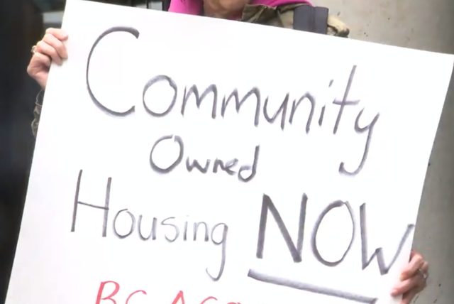 Person holding up protest sign reading "Community owned housing NOW"