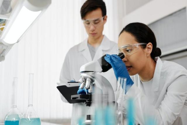 Two researchers in white lab coats working with one looking into a microscope