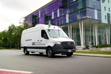 A white van equipped with air monitoring instruments drives through the streets of the UBC Campus. Decal on front passenger door reads 'UBC Department of Mechanical Engineering'