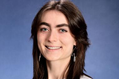 Lucy Myrol smiles for the camera, centered in front of a blue photo backdrop