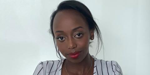 A headshot photo of Ashley Kairu, centered, as she softly smiles at the camera.
