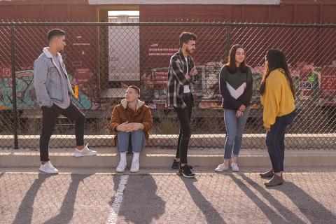 Five youth standing in front of a school barbed wire fence and talking to each other