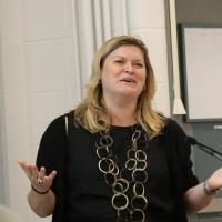 Woman in large ornate necklace speaking at lectern