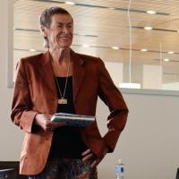 Woman in orange blazer holding notes in one hand and other hand on hip
